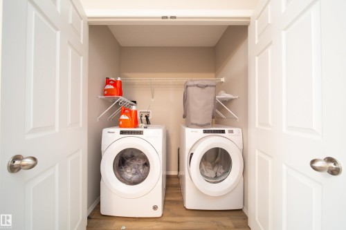 Dedicated laundry area featuring a washer and dryer, wood-finish flooring, and integrated wire shelving for storage - 3038 Checknita Way Sw, Edmonton, AB 