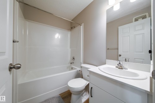 Bathroom featuring a white vanity with integrated sink, chrome faucet, and a large wall-mounted mirror - 3038 Checknita Way Sw, Edmonton, AB 