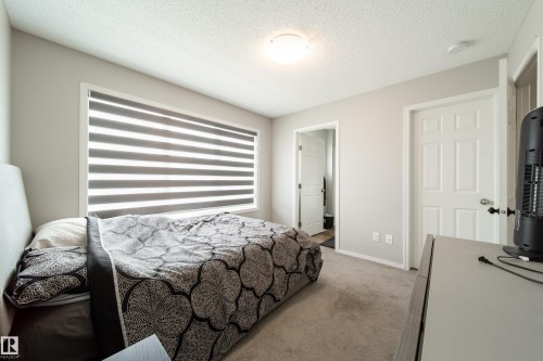 Carpeted room featuring a large window with horizontal blinds, neutral wall paint, white trim, and a flush mount ceiling light - 3038 Checknita Way Sw, Edmonton, AB 