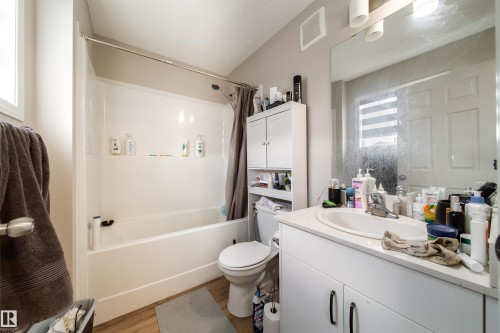 Bathroom featuring a combined tub and shower unit, a white vanity with an integrated sink, and wood-finish flooring - 3038 Checknita Way Sw, Edmonton, AB 