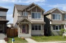 Two-story residence featuring a covered front porch with a red entry door, horizontal siding, and gable roof accents - 3038 Checknita Way Sw, Edmonton, AB 