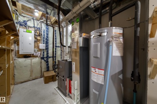 Utility space featuring a water heater, furnace, electrical panel, and exposed ductwork - 3038 Checknita Way Sw, Edmonton, AB 