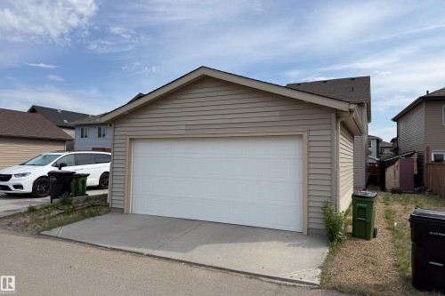 Detached garage featuring horizontal siding, a white sectional overhead door, and a concrete approach - 3038 Checknita Way Sw, Edmonton, AB 