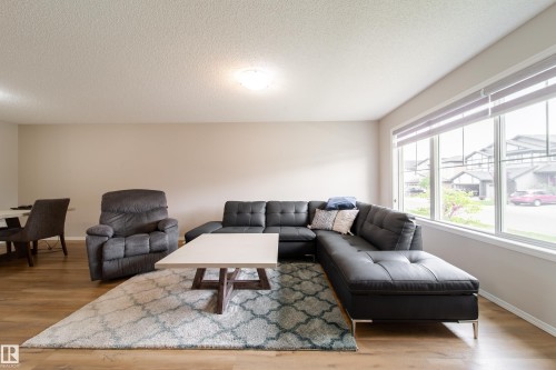 Spacious living area featuring wood-finish flooring, neutral wall tones, and a large window array with roller shades - 3038 Checknita Way Sw, Edmonton, AB 