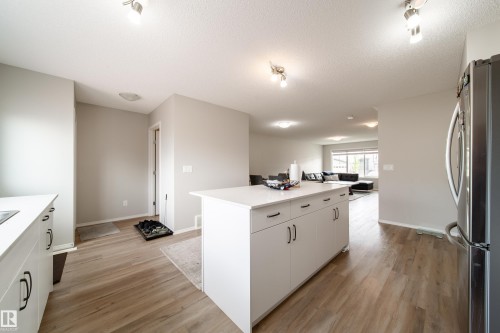 Kitchen featuring a central island with white cabinetry and dark hardware, light-toned countertops, and wood-finish flooring - 3038 Checknita Way Sw, Edmonton, AB 