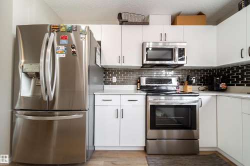Modern kitchen featuring white cabinetry, stainless steel appliances, a black subway tile backsplash, and light countertops - 3038 Checknita Way Sw, Edmonton, AB 