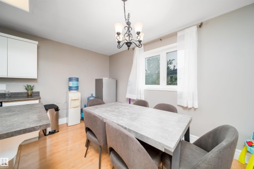 Dining area featuring a modern light fixture, wood-finish flooring, and a large window - 8512 142A Avenue, Edmonton, AB 
