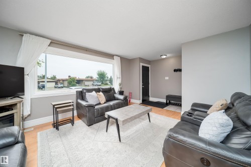 Spacious living area featuring light gray wall tones, wood-finish flooring, and a large picture window - 8512 142A Avenue, Edmonton, AB 