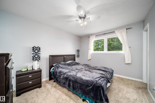 Carpeted bedroom featuring a large window, a ceiling fan with integrated lighting, and a solid-panel door - 8512 142A Avenue, Edmonton, AB 