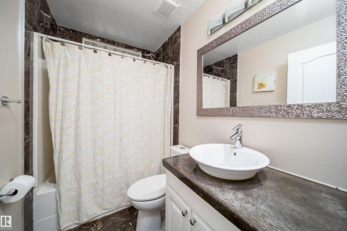 Bathroom featuring a white vanity with a vessel sink, a coordinating dark countertop, and a large framed mirror - 8512 142A Avenue, Edmonton, AB 