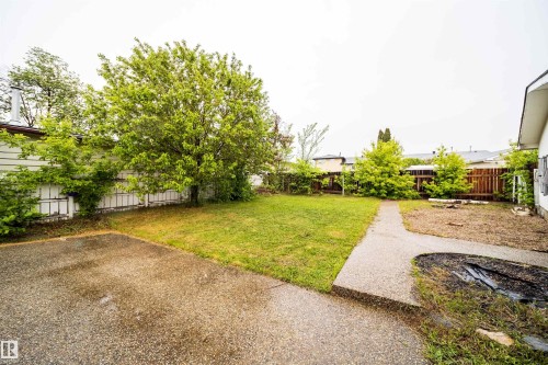 Expansive backyard featuring a large paved patio, a manicured lawn, a concrete pathway, a privacy fence, and mature landscaping - 8512 142A Avenue, Edmonton, AB 