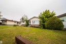 Expansive front lawn with mature landscaping, a brick garden wall, and a single-story residence featuring white siding and a stone-clad foundation - 8512 142A Avenue, Edmonton, AB 