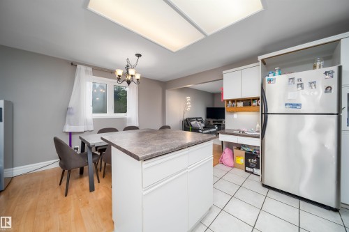 Kitchen featuring an island with a stone-finish countertop, white cabinetry, a stainless steel refrigerator, and recessed lighting - 8512 142A Avenue, Edmonton, AB 