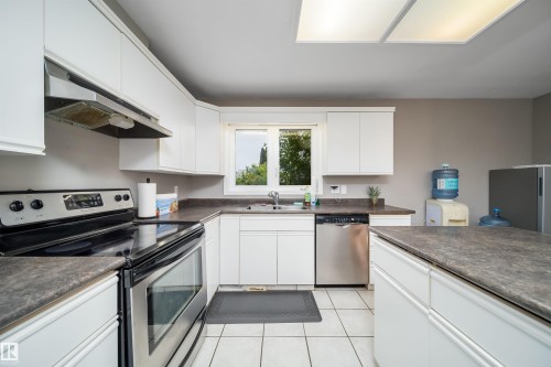 Kitchen featuring white cabinetry, dark countertops, white tile flooring, stainless steel appliances, and an island - 8512 142A Avenue, Edmonton, AB 