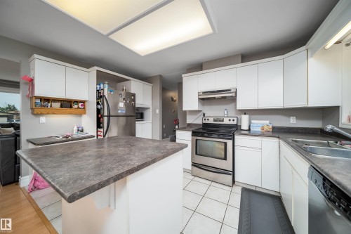 Kitchen featuring white cabinetry, dark countertops, stainless steel appliances, a center island, and tiled flooring - 8512 142A Avenue, Edmonton, AB 