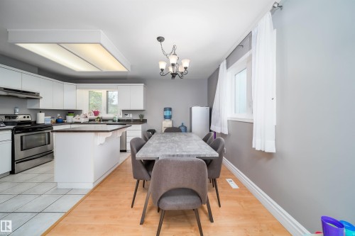 Open concept kitchen and dining area featuring a full suite of stainless steel appliances, white cabinetry, dark countertops, and an island - 8512 142A Avenue, Edmonton, AB 