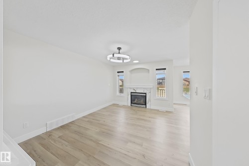 Spacious living area featuring light wood-finish flooring, a contemporary fireplace with a marble-look surround, an arched alcove, and modern ceiling light fixture - 6144 166 Avenue, Edmonton, AB 