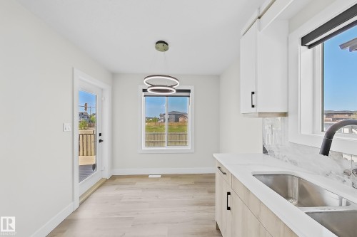 Modern kitchen area featuring light wood-finish flooring, white cabinetry, and a stainless steel sink with a matte black faucet - 6144 166 Avenue, Edmonton, AB 
