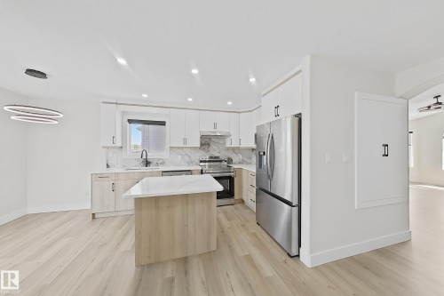 Contemporary kitchen featuring light wood-finish flooring, white cabinetry, stainless steel appliances, and a central island with a white countertop - 6144 166 Avenue, Edmonton, AB 