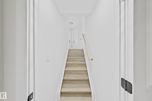 Staircase featuring wood-finish treads, a light wood handrail, and white risers - 6144 166 Avenue, Edmonton, AB 