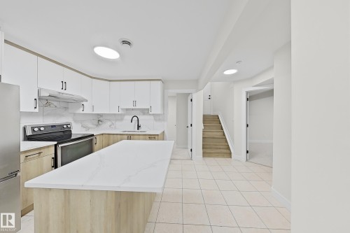 Modern kitchen featuring an expansive island with a quartz countertop, two-tone cabinetry, stainless steel appliances, and a marble-patterned backsplash - 6144 166 Avenue, Edmonton, AB 