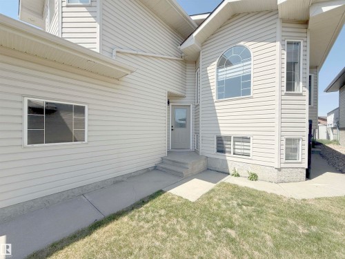 Exterior featuring light-colored horizontal siding, a prominent arched window, multiple rectangular windows, a neutral-toned entry door, and concrete pathways - 6144 166 Avenue, Edmonton, AB 
