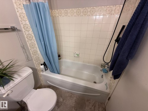White bathtub and shower combination featuring a tiled surround with decorative accent border - 304 10604 110 Avenue, Edmonton, AB 
