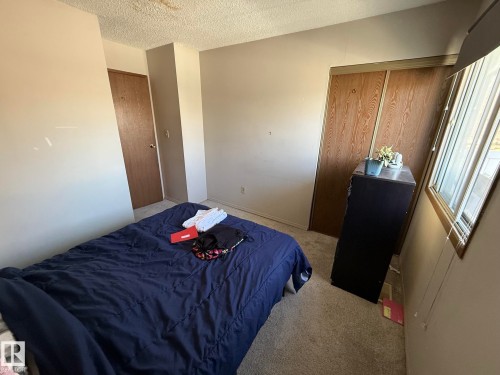 Interior room featuring neutral wall paint, textured ceiling, a window with blinds, and wood-finish bifold closet doors - 304 10604 110 Avenue, Edmonton, AB 