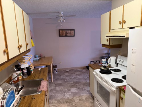 Kitchen area featuring wood-finish countertops, white cabinetry with wood-tone accents, a built-in electric range, and an integrated stainless steel sink - 304 10604 110 Avenue, Edmonton, AB 