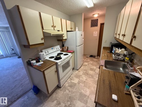 Kitchen featuring a stainless steel sink, wood-finish countertops, white cabinetry with round hardware, and a white oven range - 304 10604 110 Avenue, Edmonton, AB 