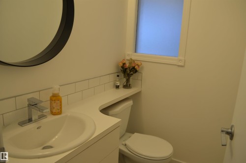 Compact bathroom featuring a white vanity with integrated sink, chrome faucet, and a round wall-mounted mirror - 68 Marlboro Road, Edmonton, AB 