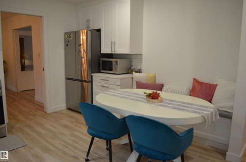 Kitchen featuring light wood-finish flooring, white cabinetry with silver hardware, a built-in banquette, and a subway tile backsplash - 68 Marlboro Road, Edmonton, AB 