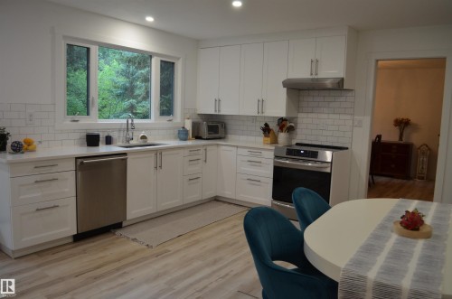 Kitchen featuring white shaker-style cabinetry with brushed nickel hardware, stainless steel appliances, a subway tile backsplash, and light wood-finish flooring - 68 Marlboro Road, Edmonton, AB 