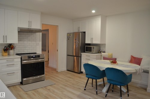 Modern kitchen featuring white shaker cabinetry, stainless steel appliances, a subway tile backsplash, and light wood-finish flooring - 68 Marlboro Road, Edmonton, AB 