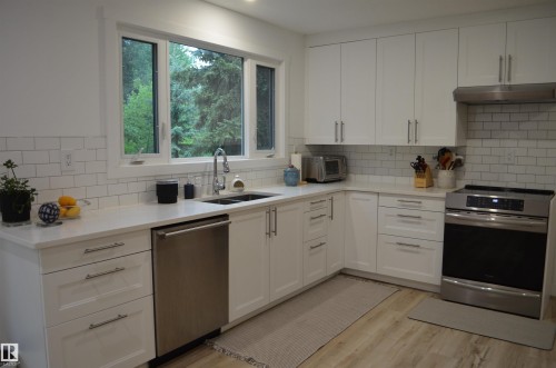 Contemporary kitchen featuring white shaker-style cabinetry, white subway tile backsplash, stainless steel appliances, and wood-finish flooring - 68 Marlboro Road, Edmonton, AB 