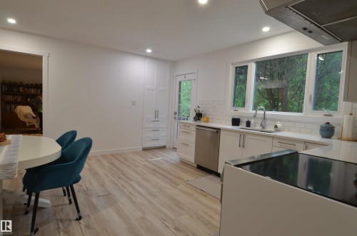 Bright kitchen featuring wood-finish flooring, white cabinetry, integrated stainless steel appliances, a subway tile backsplash, and recessed lighting - 68 Marlboro Road, Edmonton, AB 