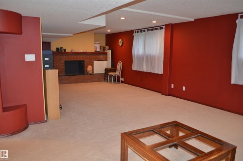 Spacious finished lower level featuring a brick fireplace surround, light-colored carpeting, recessed lighting, and multiple windows - 68 Marlboro Road, Edmonton, AB 