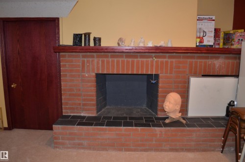 Brick fireplace featuring a tiled hearth, wood mantel, and an adjacent wood-paneled door - 68 Marlboro Road, Edmonton, AB 