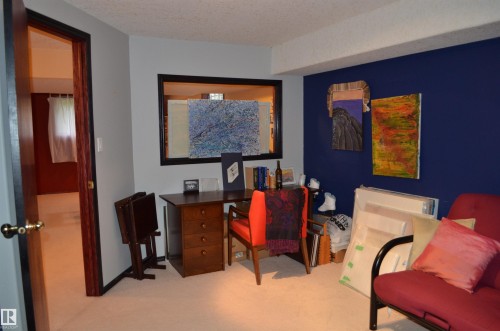 Carpeted interior space featuring a dark wood-finish desk with drawers, a large framed opening, and a contrasting accent wall - 68 Marlboro Road, Edmonton, AB 