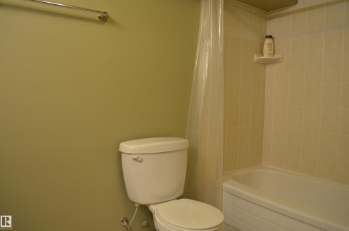 Bathroom featuring a white toilet, full bathtub with a shower, and light-toned wall tile - 68 Marlboro Road, Edmonton, AB 