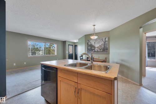 Kitchen island with a double basin stainless steel sink, a black dishwasher, and wood-finish cabinetry - 40 604 62 Street, Edmonton, AB 