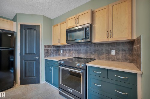 Kitchen featuring dark teal lower cabinetry, light wood-finish upper cabinetry, a black appliance suite, and a tiled backsplash - 40 604 62 Street, Edmonton, AB 