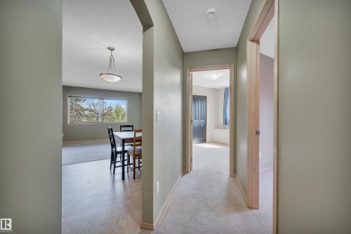 Hallway with light green walls, carpet flooring, and natural wood door frames - 40 604 62 Street, Edmonton, AB 