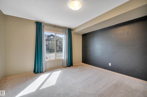 Carpeted room with a large window, neutral painted walls, and a contrasting accent wall - 40 604 62 Street, Edmonton, AB 