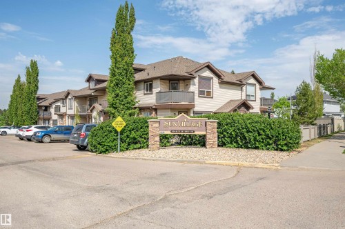 Entryway featuring a stone-clad monument sign, mature shrubbery, paved parking, and multi-story residential buildings with private balconies - 40 604 62 Street, Edmonton, AB 