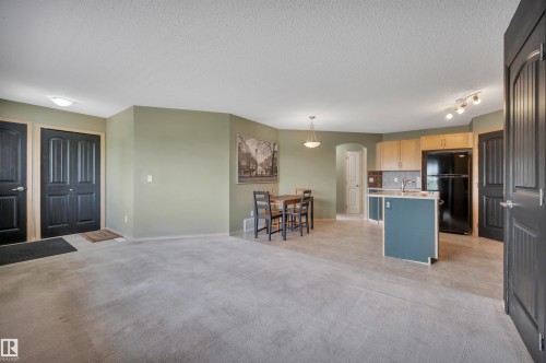 Open-concept living space featuring light carpeting, a kitchen with an island, and dark paneled doors - 40 604 62 Street, Edmonton, AB 