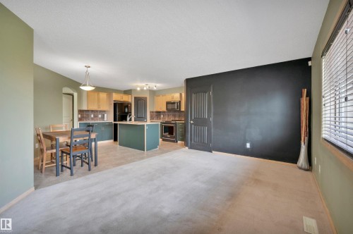 Open-concept living area with a kitchen featuring wood-finish cabinetry, a central island with sink, and dark appliances - 40 604 62 Street, Edmonton, AB 