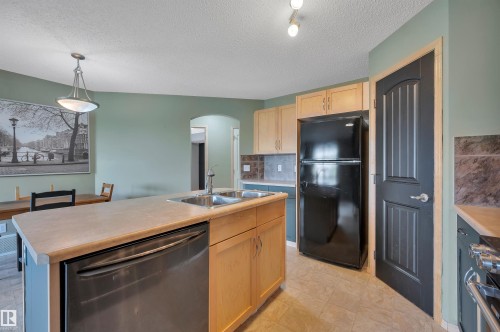 Kitchen featuring a central island with an integrated double basin sink, beige countertops, light wood-finish cabinetry, and black appliances - 40 604 62 Street, Edmonton, AB 