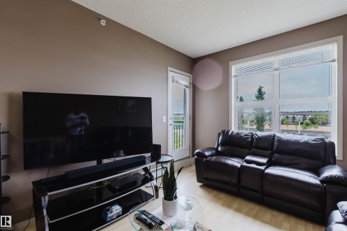 Living area with wood-finish flooring, neutral wall tones, and large windows - 1-405 4245 139 Avenue, Edmonton, AB 