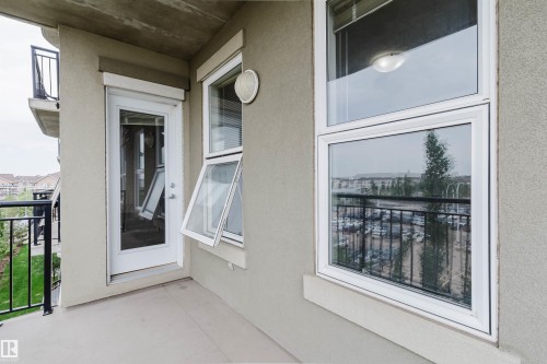 Private balcony with a concrete floor, featuring a glass-paneled door, an awning window, and a fixed window with white frames - 1-405 4245 139 Avenue, Edmonton, AB 